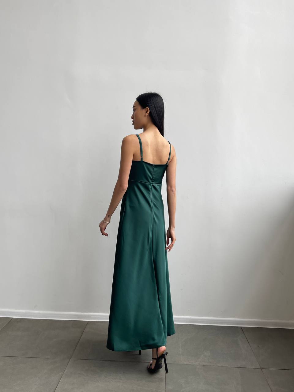 Woman wearing a green dress standing against a plain white wall.