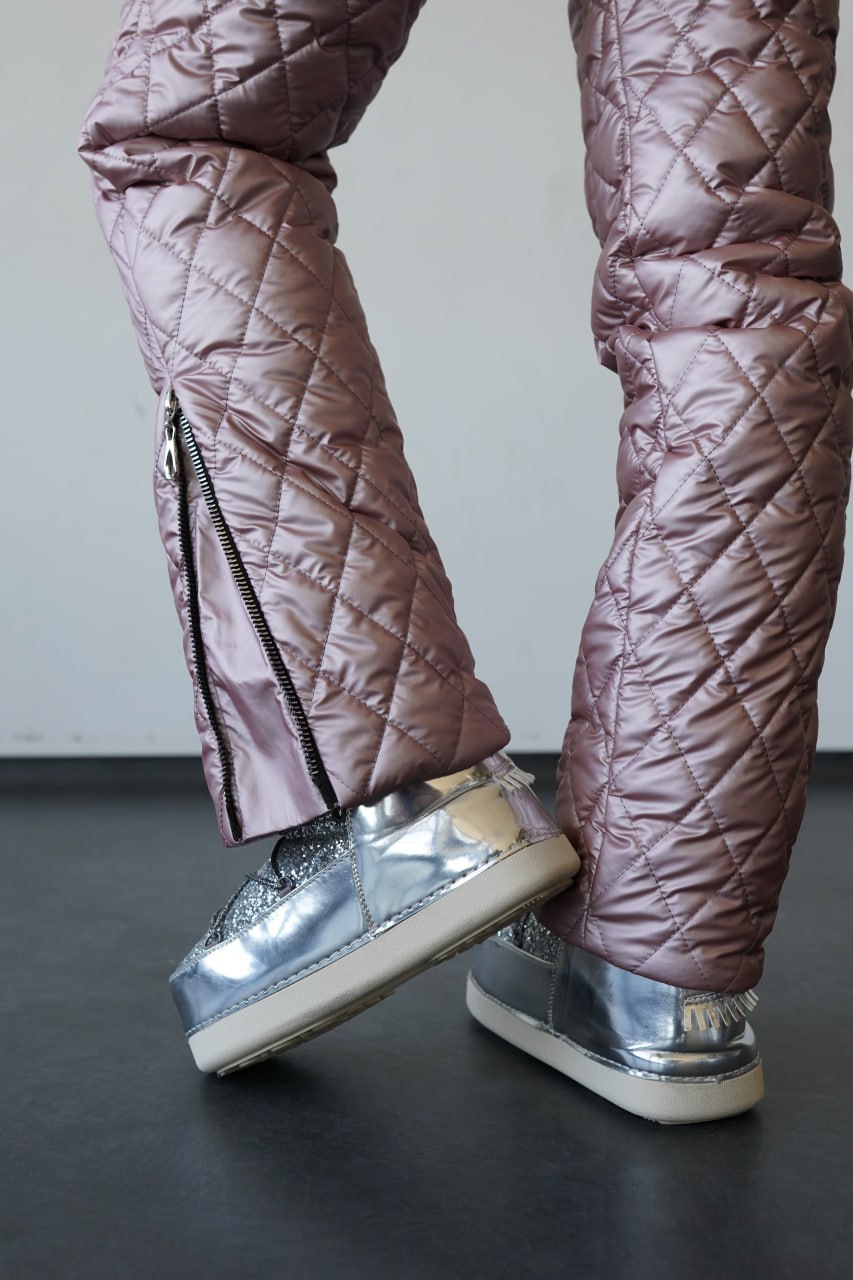 Person wearing quilted pink pants and silver shoes on a dark floor.