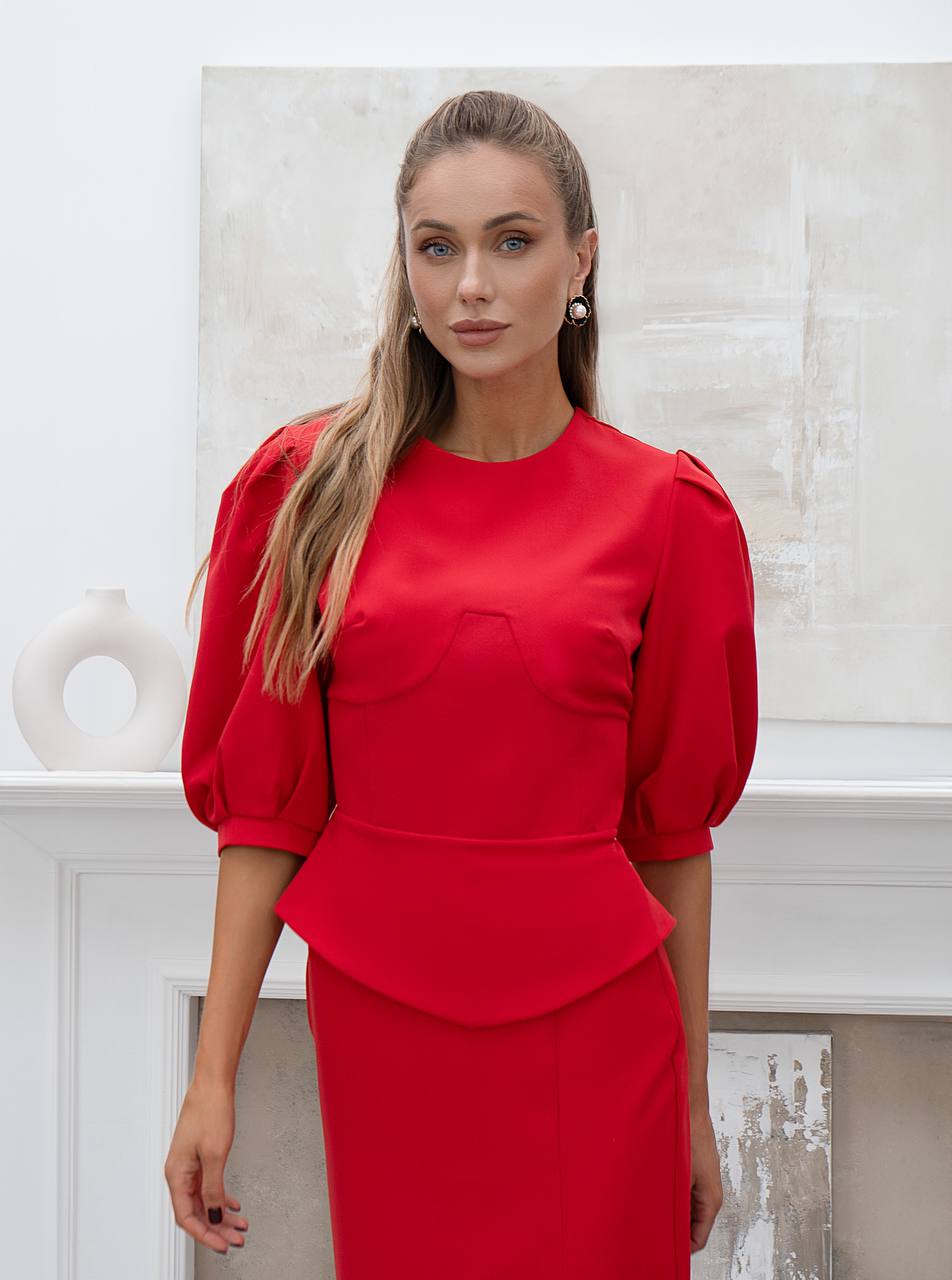 Woman wearing a red dress with puffed sleeves against a white wall.
