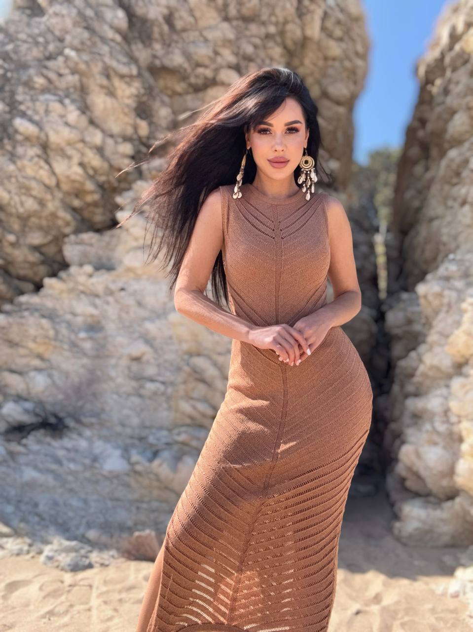 Woman in a brown dress standing against rocky cliffs.