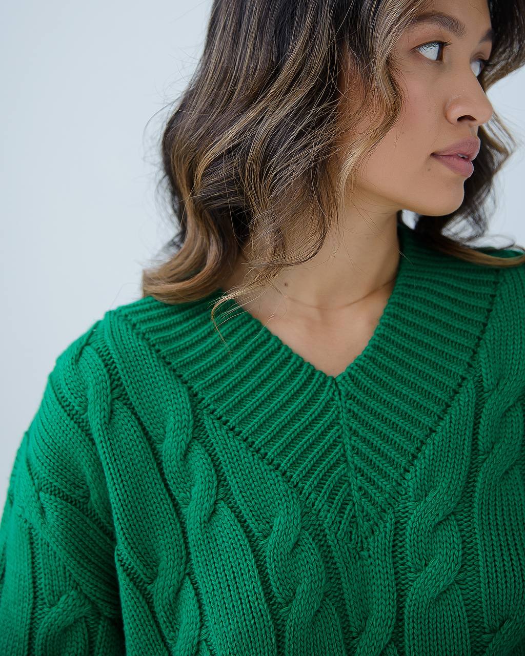 Woman wearing a green cable knit sweater against a white background