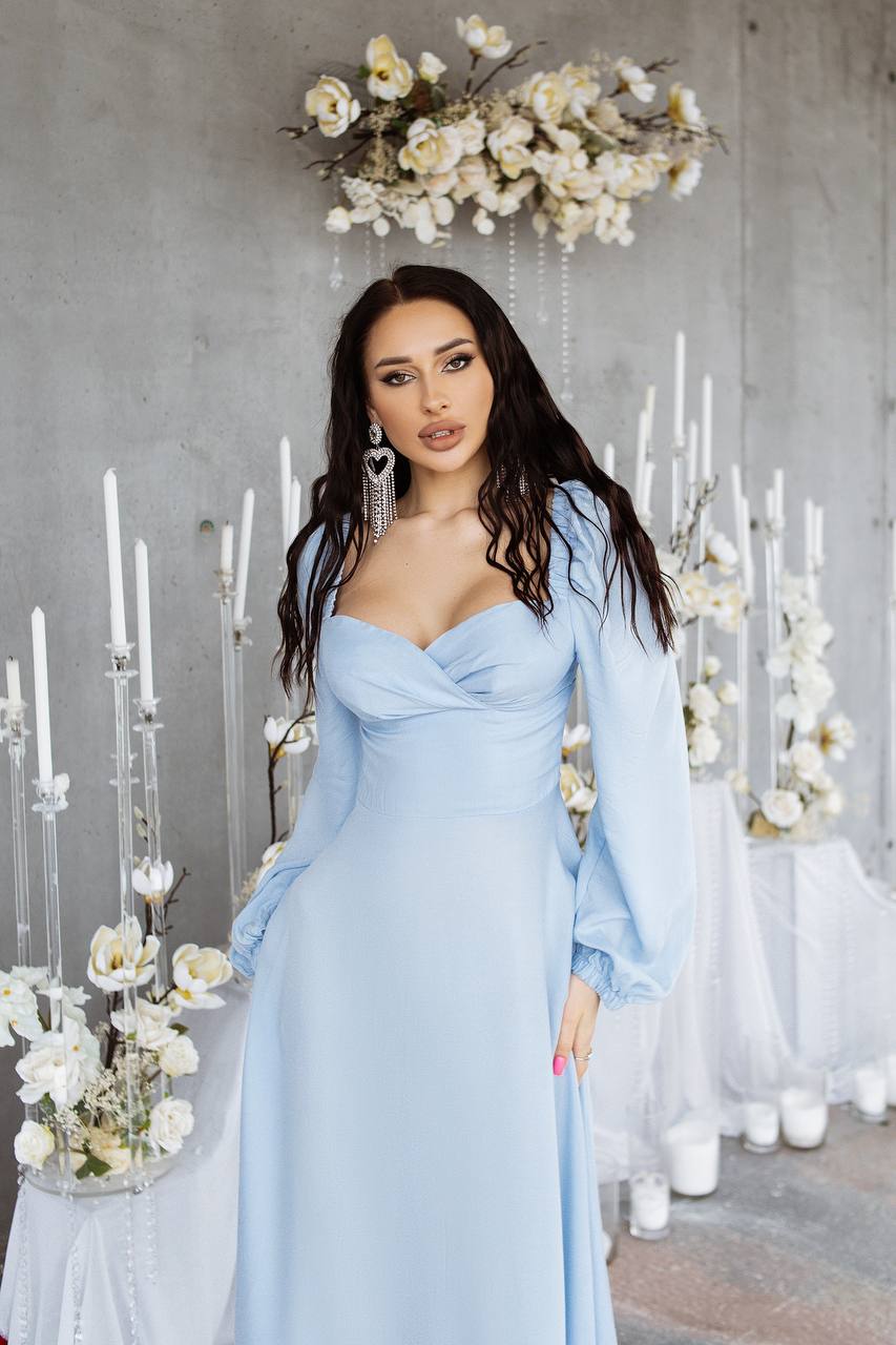Woman in a light blue dress standing in a decorated room with flowers and candles.