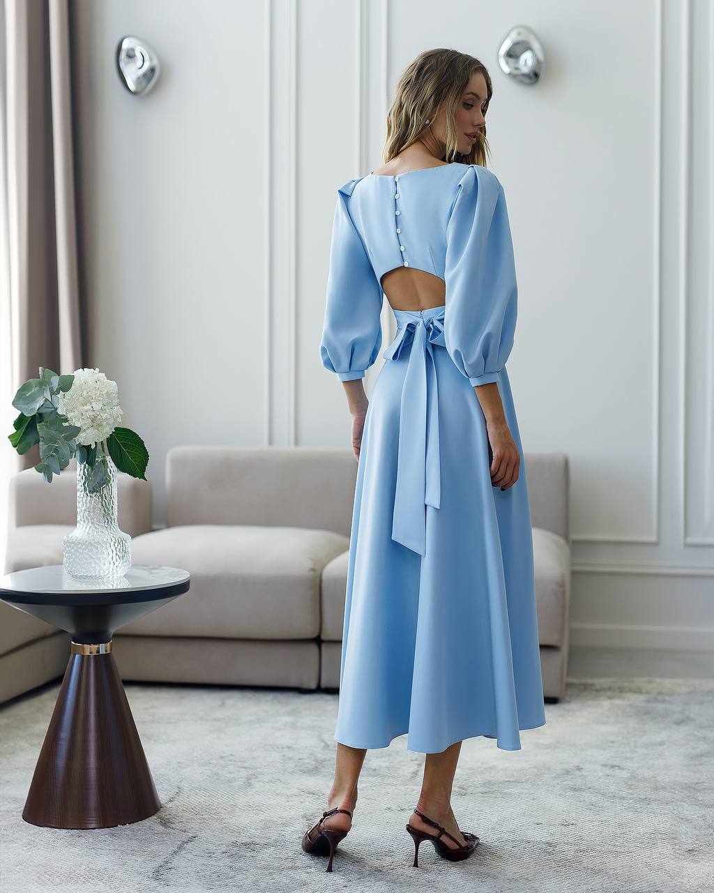 Woman wearing a light blue dress with a cutout back in an elegant room.