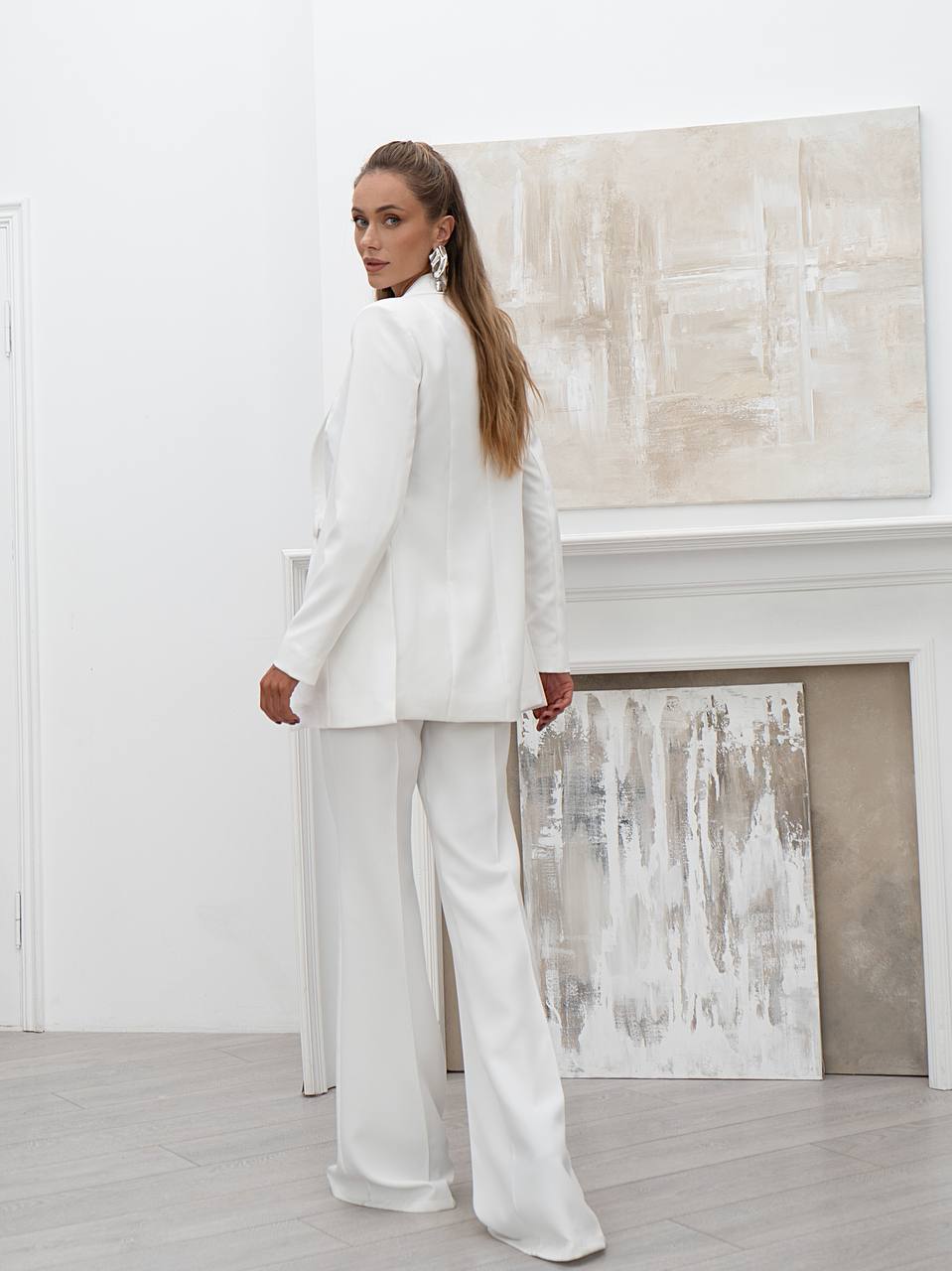 Woman in a white suit standing in a room with abstract art on the wall.