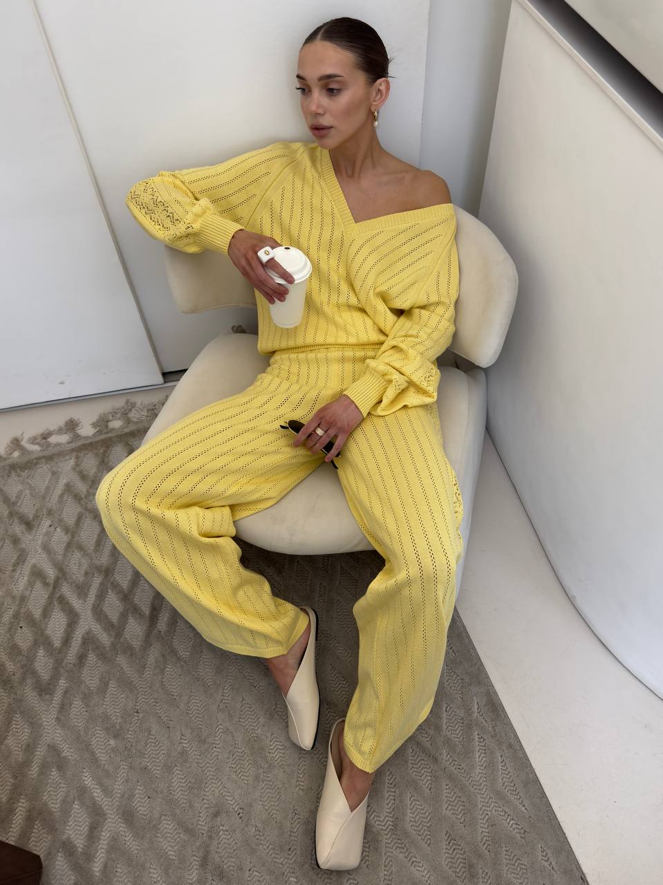 Woman in a yellow outfit sitting on a white chair indoors.