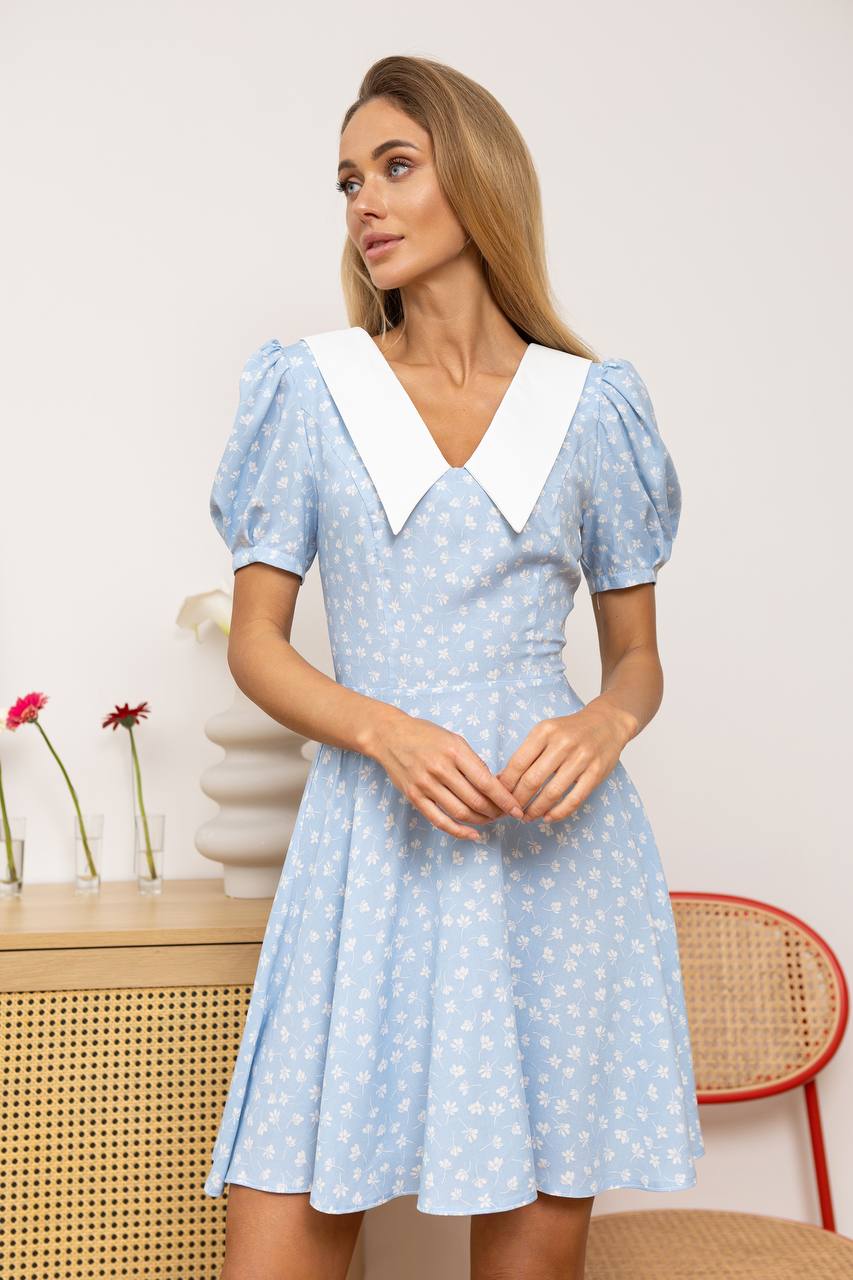 Woman wearing a light blue dress with white collar and polka dot pattern in a room setting.
