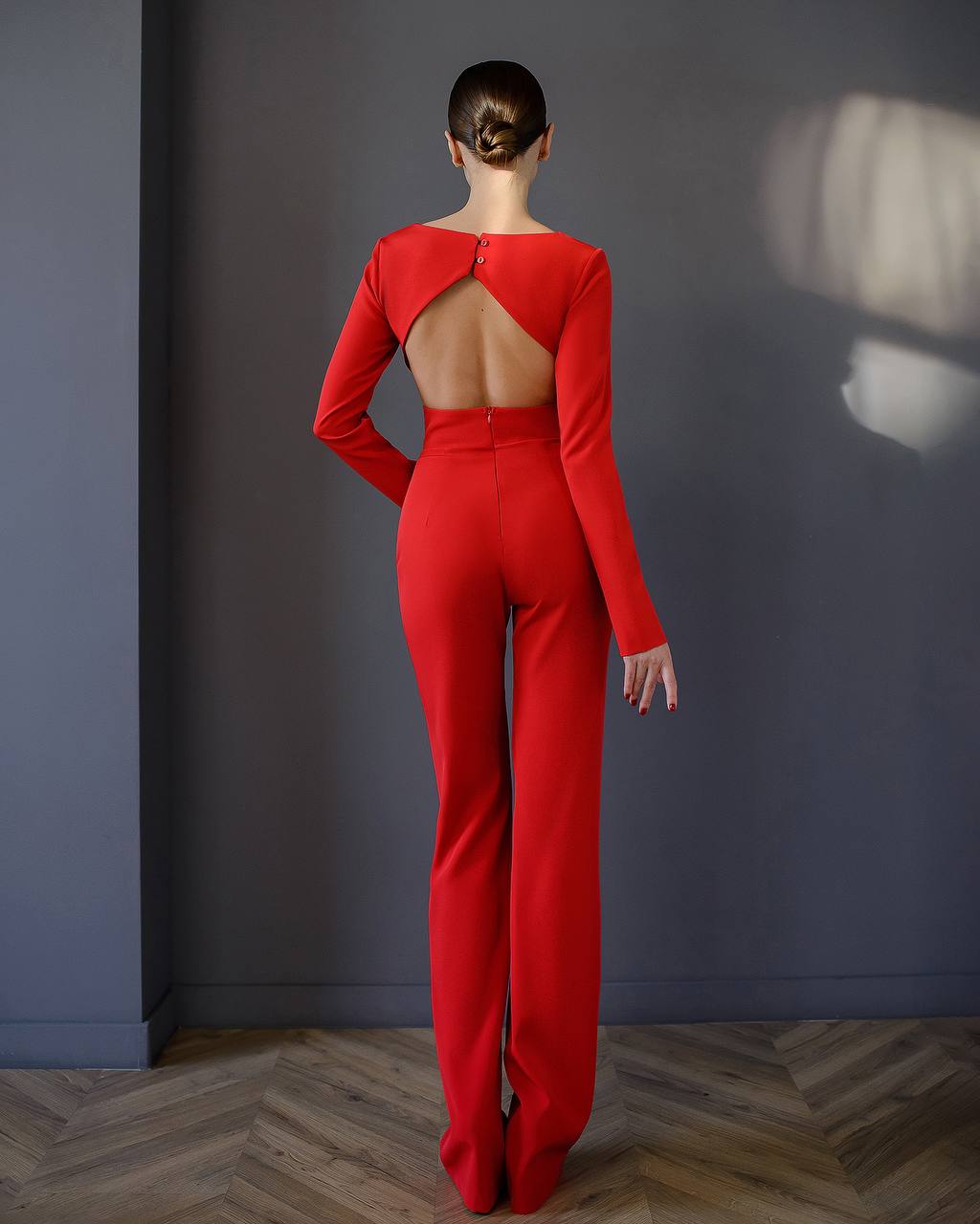 Person wearing a red jumpsuit with an open back against a gray wall.