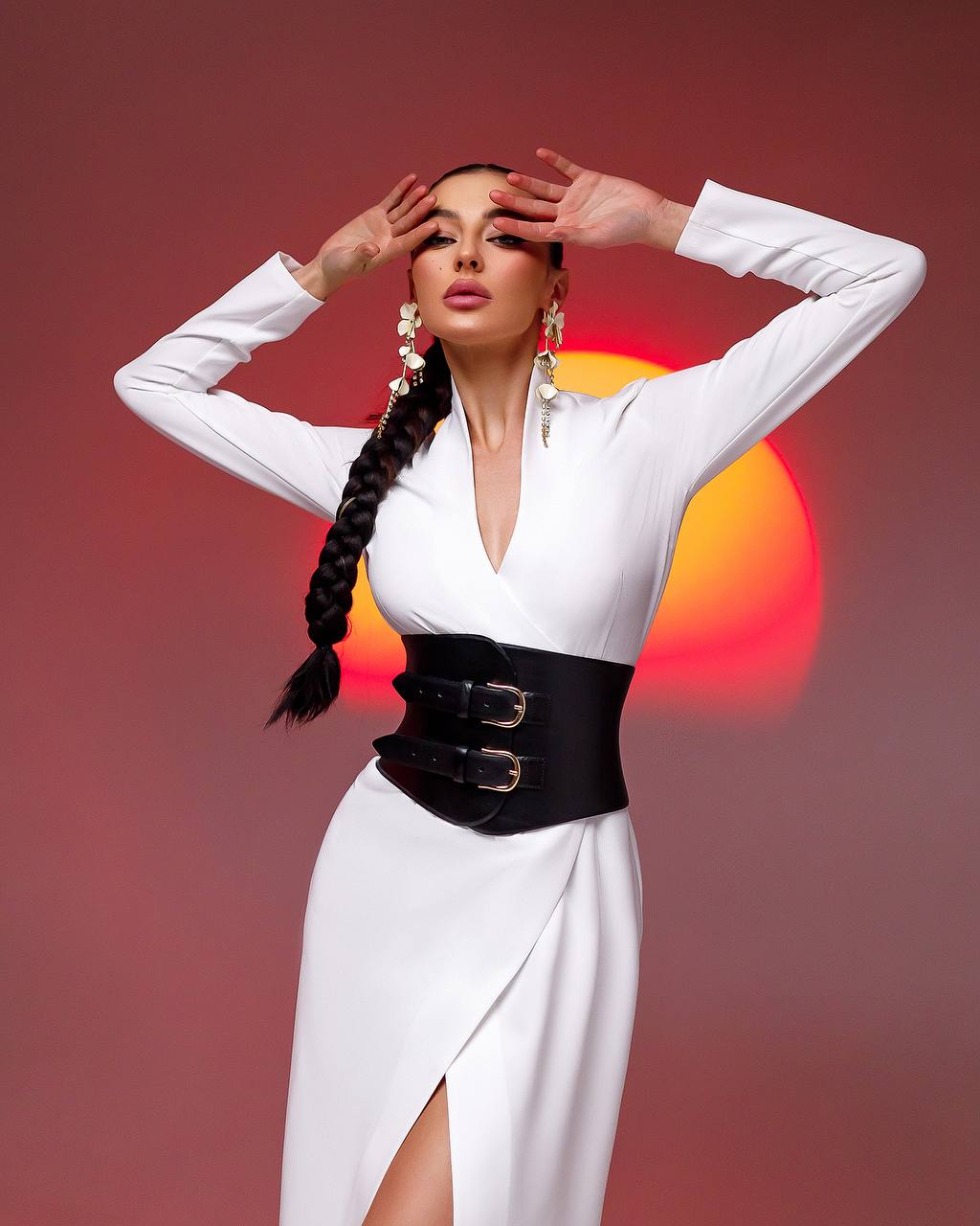 Woman in a white dress with a black waistband against a red background
