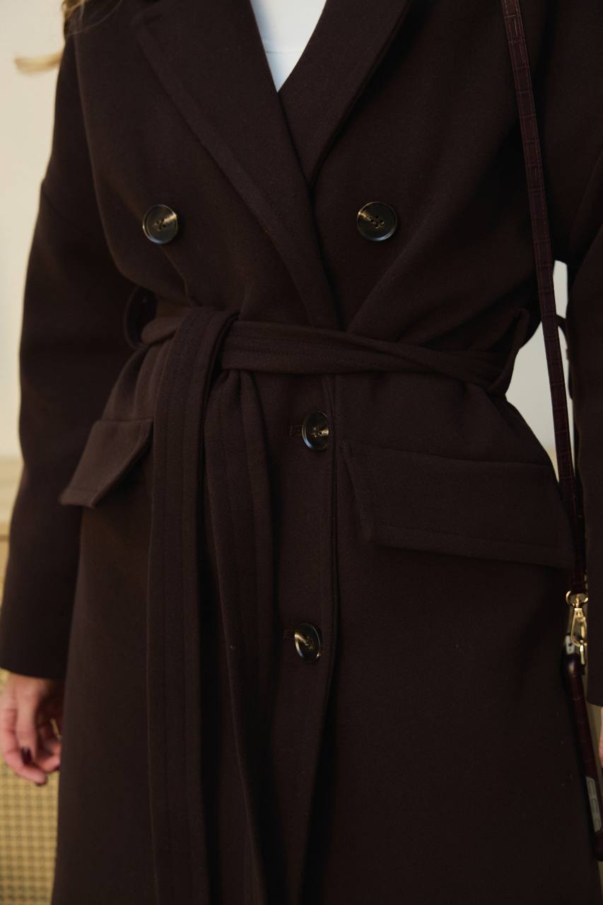 Brown trench coat with a belt and buttons on a plain background