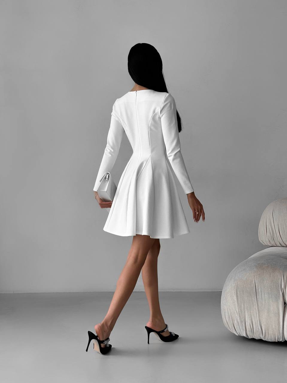 Woman wearing a white dress with long sleeves against a gray background