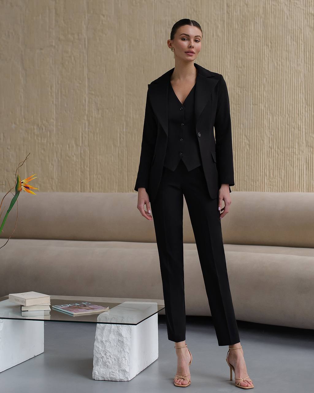 Woman in a black suit standing in a modern living room.