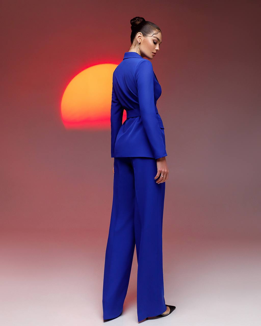 Woman in a blue suit standing against a gradient background with a colorful sun.