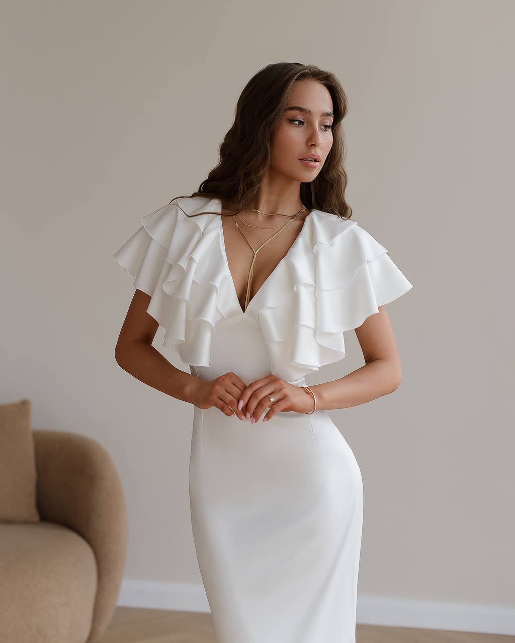 Woman wearing a white dress with ruffled sleeves against a neutral background