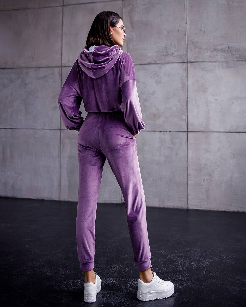 Person wearing a purple tracksuit standing against a gray wall.