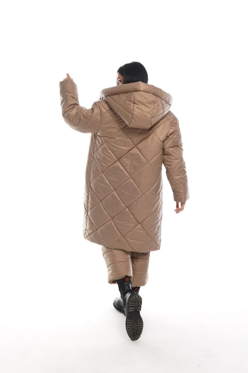 Person wearing a long beige quilted coat on a white background
