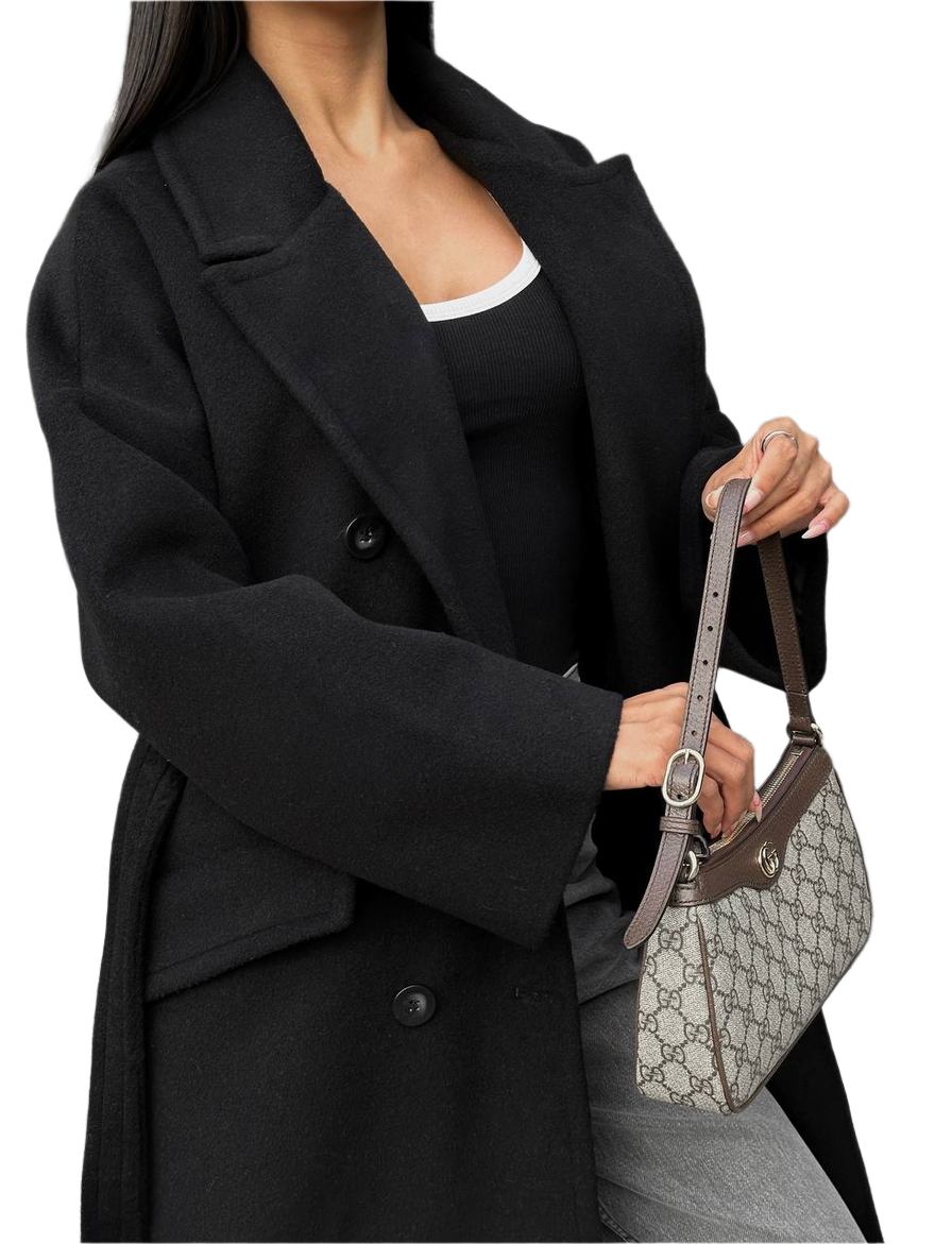 Person wearing a black coat holding a Gucci handbag on a white background