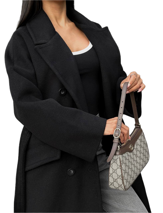 Person wearing a black coat holding a Gucci handbag on a white background
