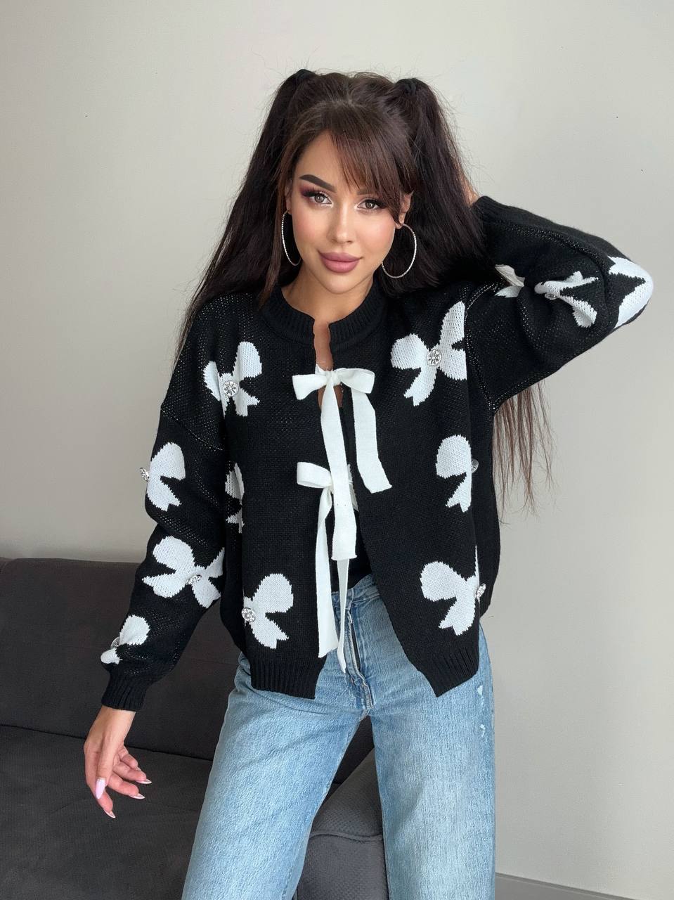 Woman wearing a black cardigan with white bow patterns and light blue jeans.