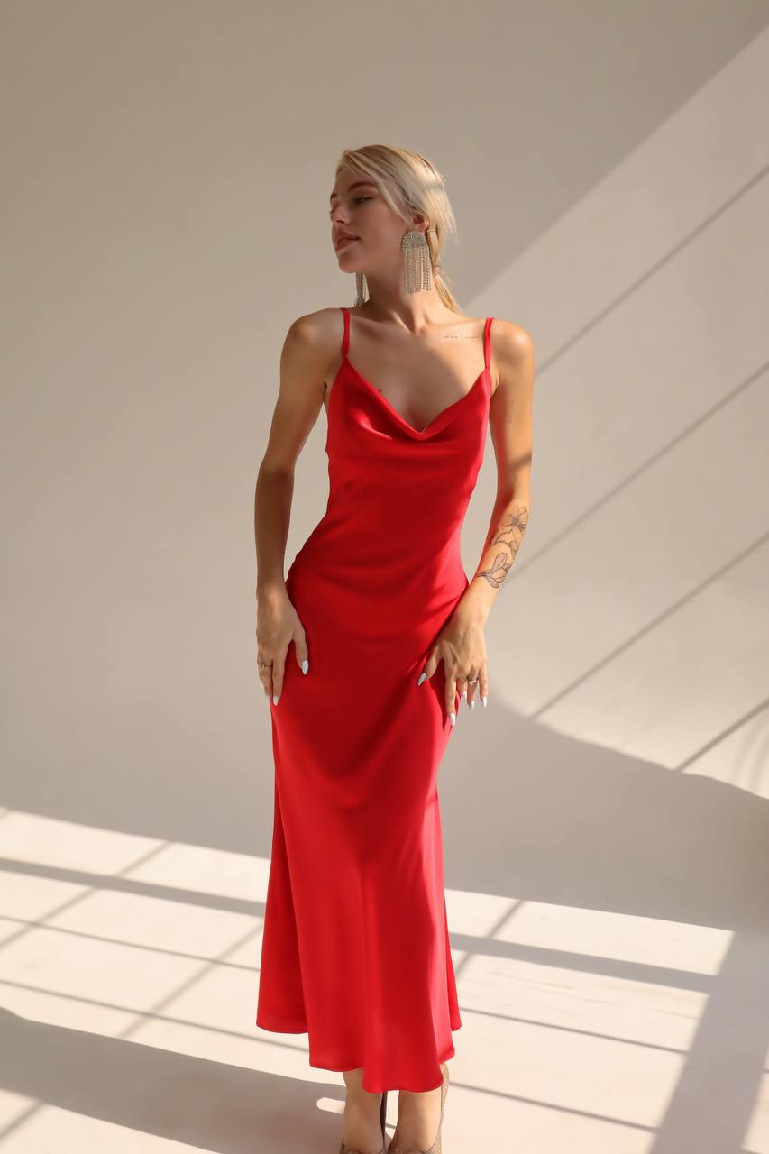Woman wearing a red dress standing in a well-lit room with sunlight casting shadows.