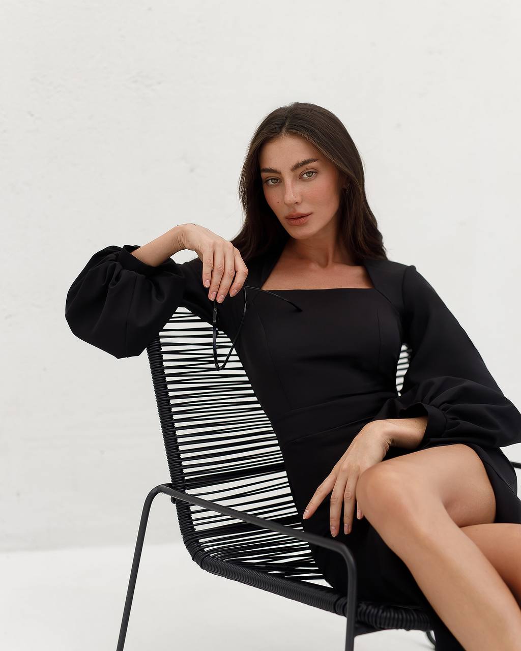Woman in a black outfit sitting on a modern chair with a white background