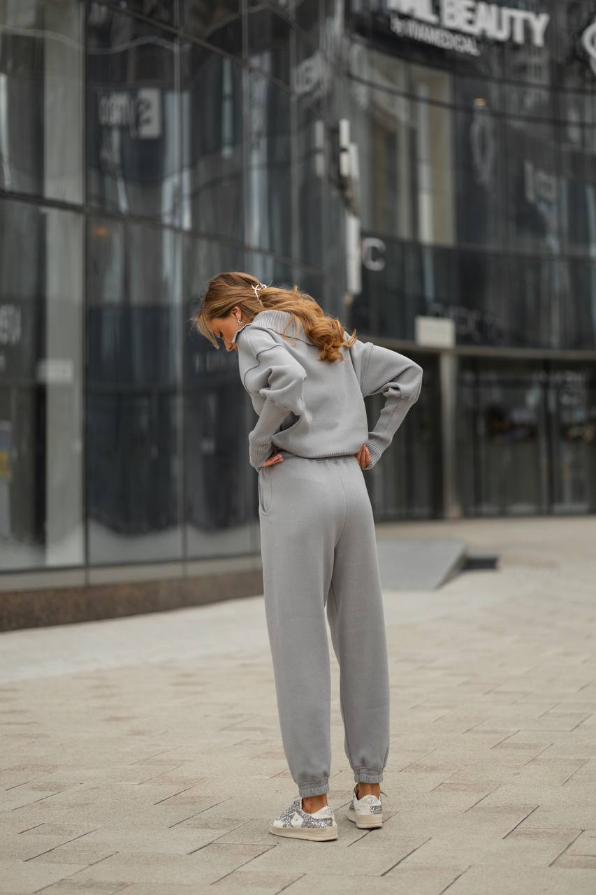 Person wearing a gray tracksuit standing on a sidewalk with a building in the background