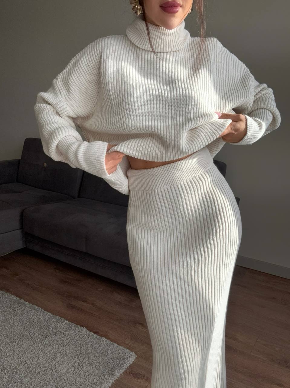 Person wearing a white ribbed knit outfit in a room with a gray sofa.