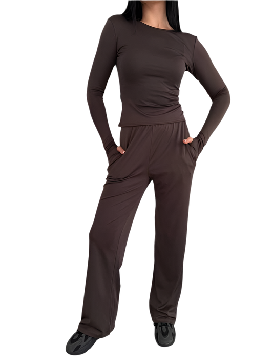 Person wearing a brown long-sleeve top and pants on a white background