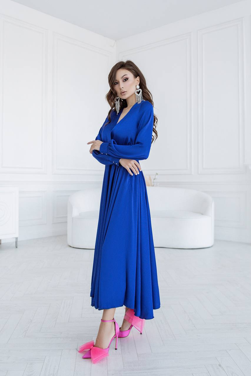 Woman in a blue dress with pink shoes standing in a white room.
