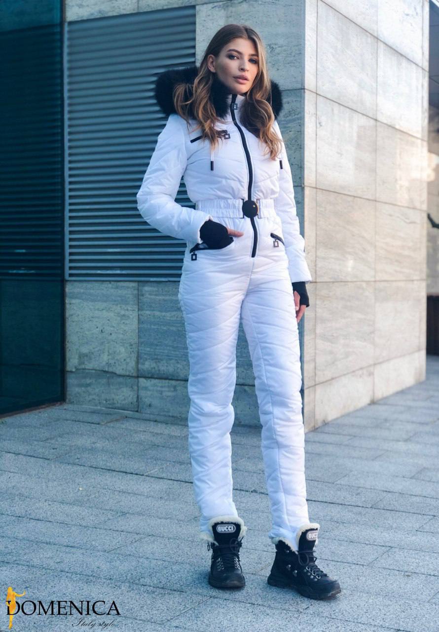 Woman in a white snowsuit standing outdoors with a building in the background