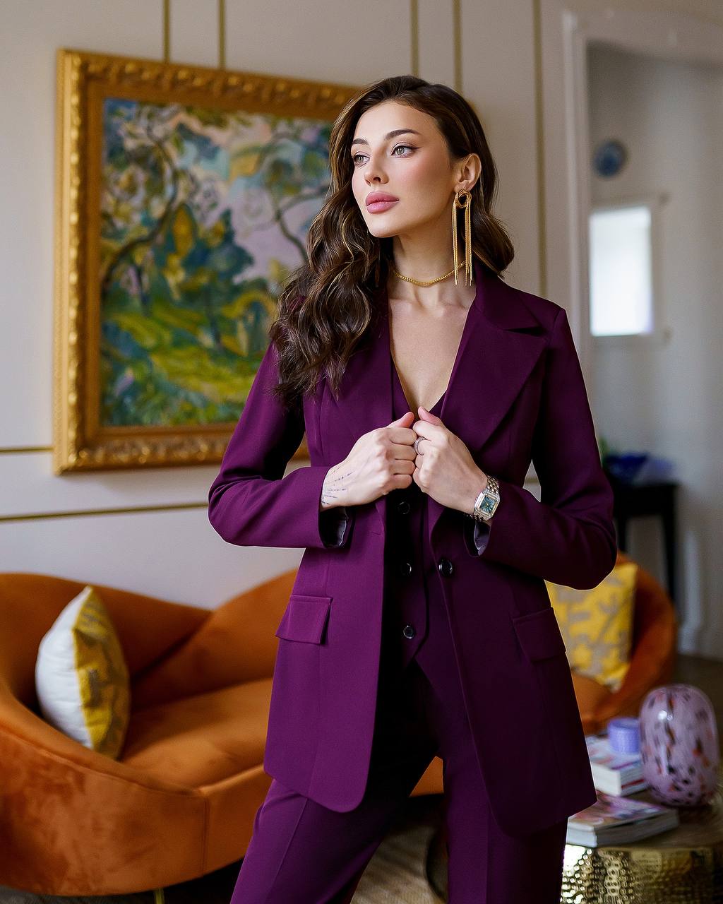 Woman in a purple suit standing in a stylish room with a painting and couch.