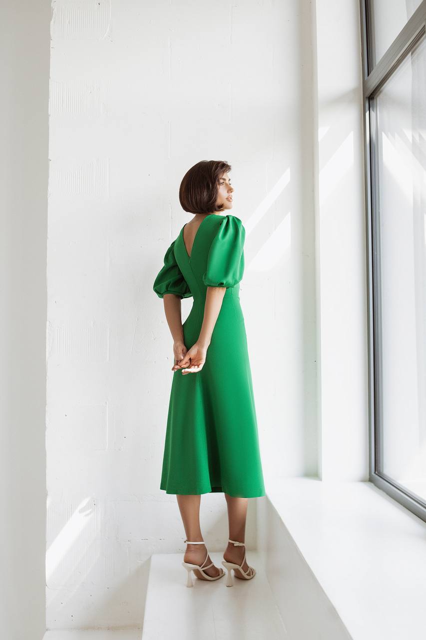Woman in a green dress standing in a bright room with large windows.