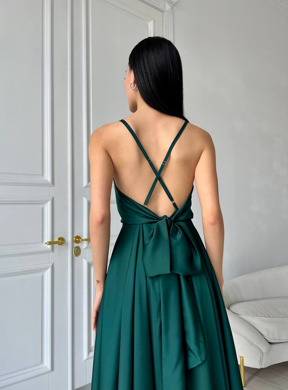 Woman wearing a green dress with a back bow, standing in a room with a white door and bed.