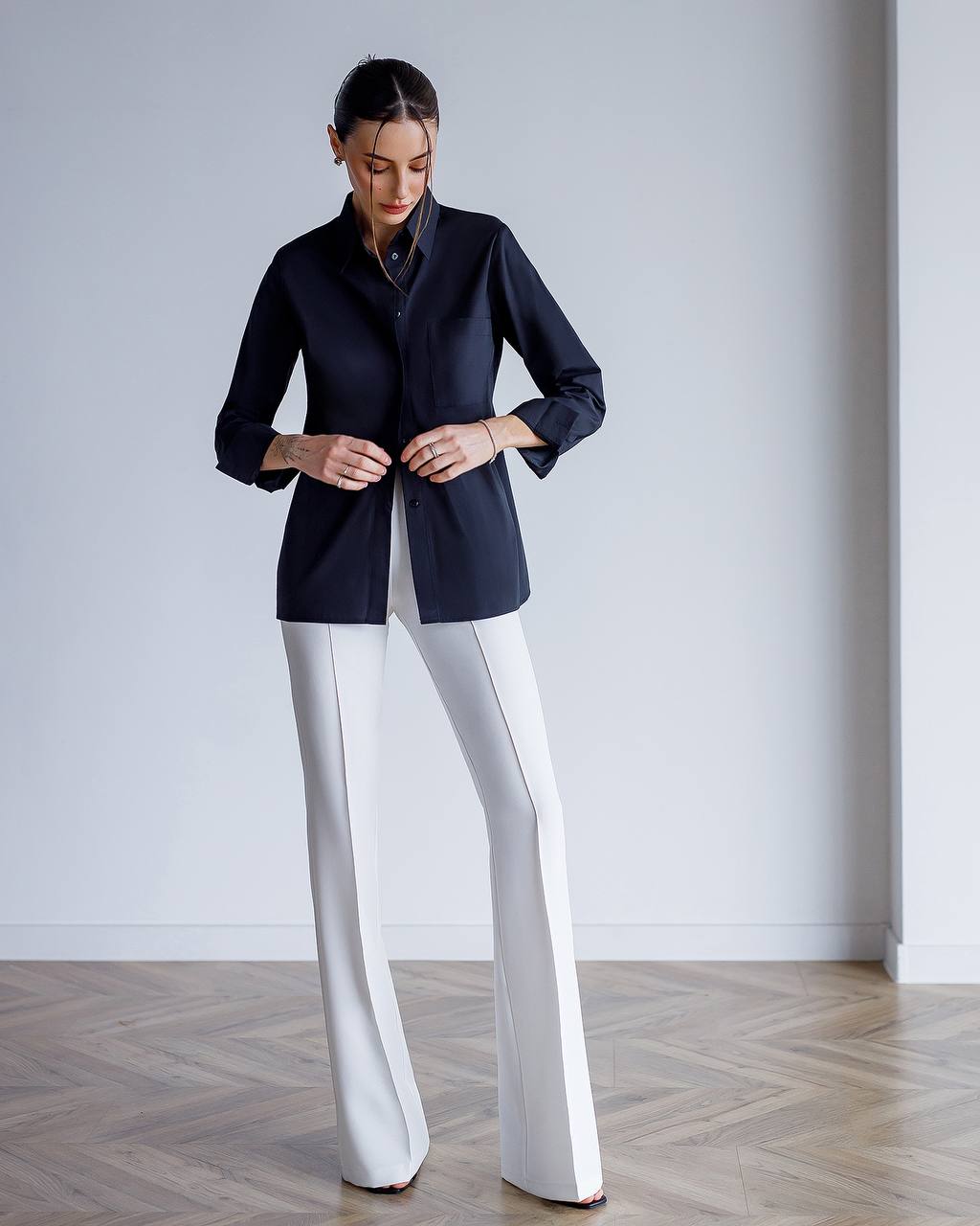Woman wearing a dark blue blazer and white pants in a minimalistic setting