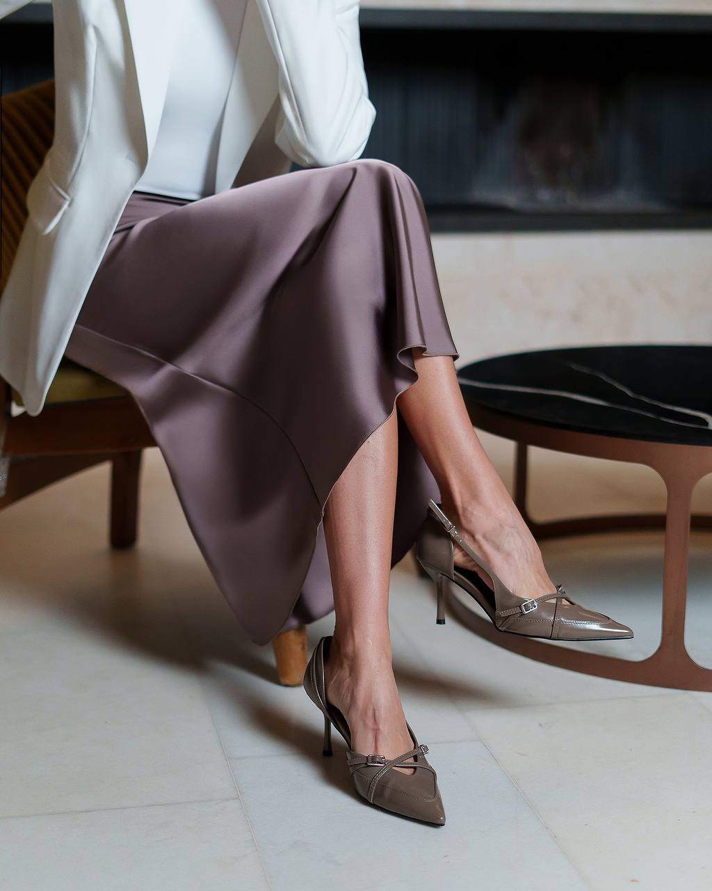 Person wearing a white blazer, purple skirt, and brown high heels in an indoor setting.