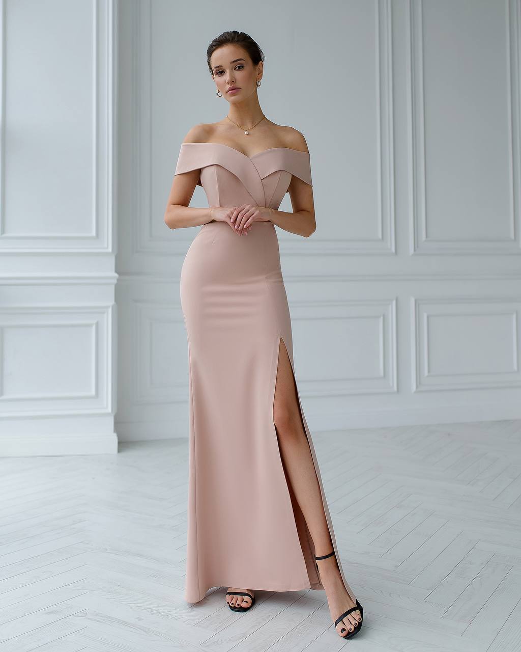 Woman wearing a pink off-shoulder gown with a slit in a white room.