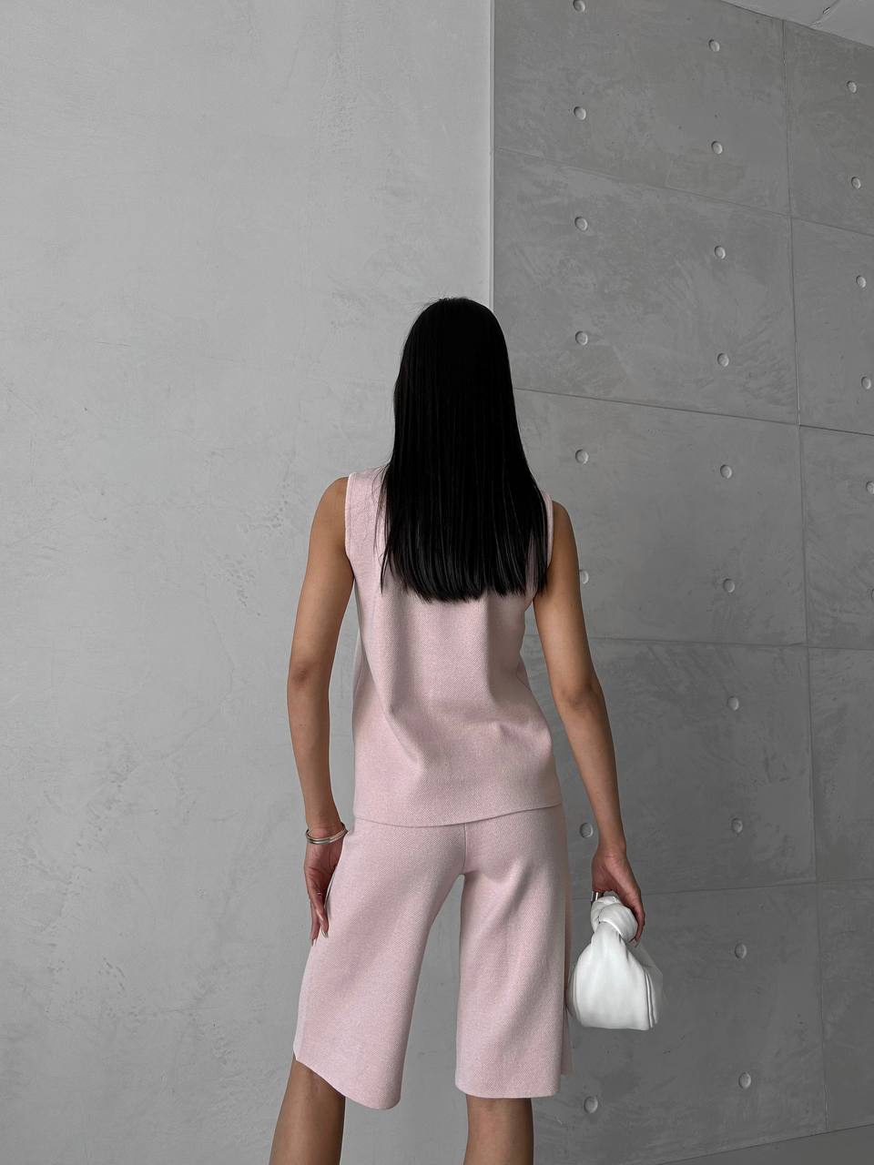 Person wearing a pink outfit standing against a gray wall.