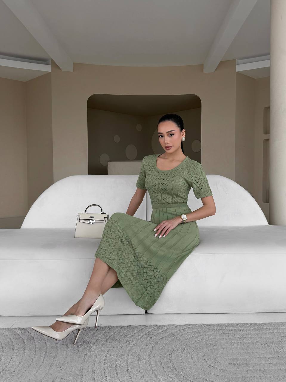 Woman in a green dress sitting on a white couch in a modern room.