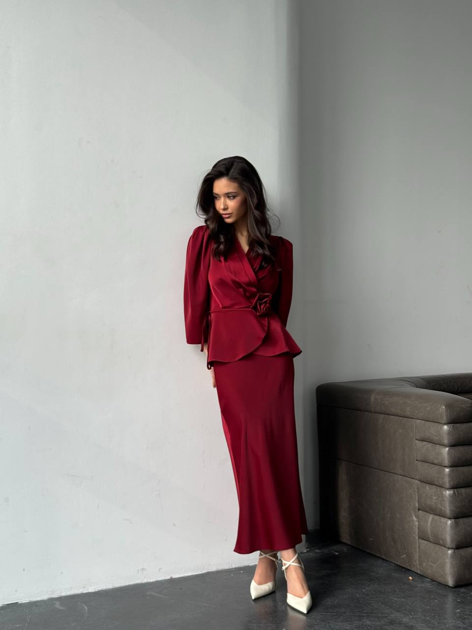 Woman in a burgundy outfit standing against a gray wall.