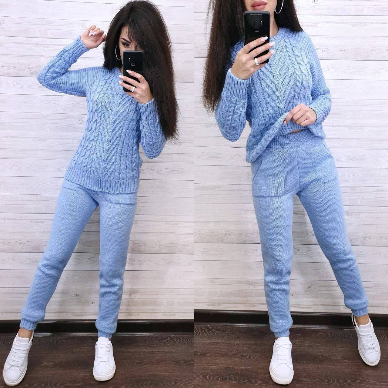 Woman wearing a light blue cable knit sweater and pants, standing in front of a mirror.