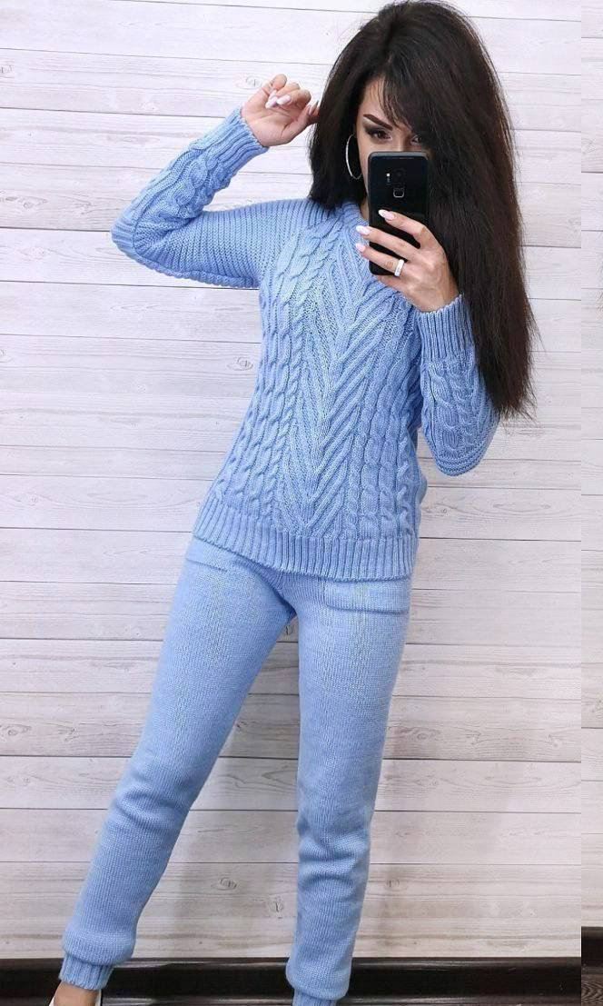 Woman wearing a light blue cable knit sweater and pants against a wooden background