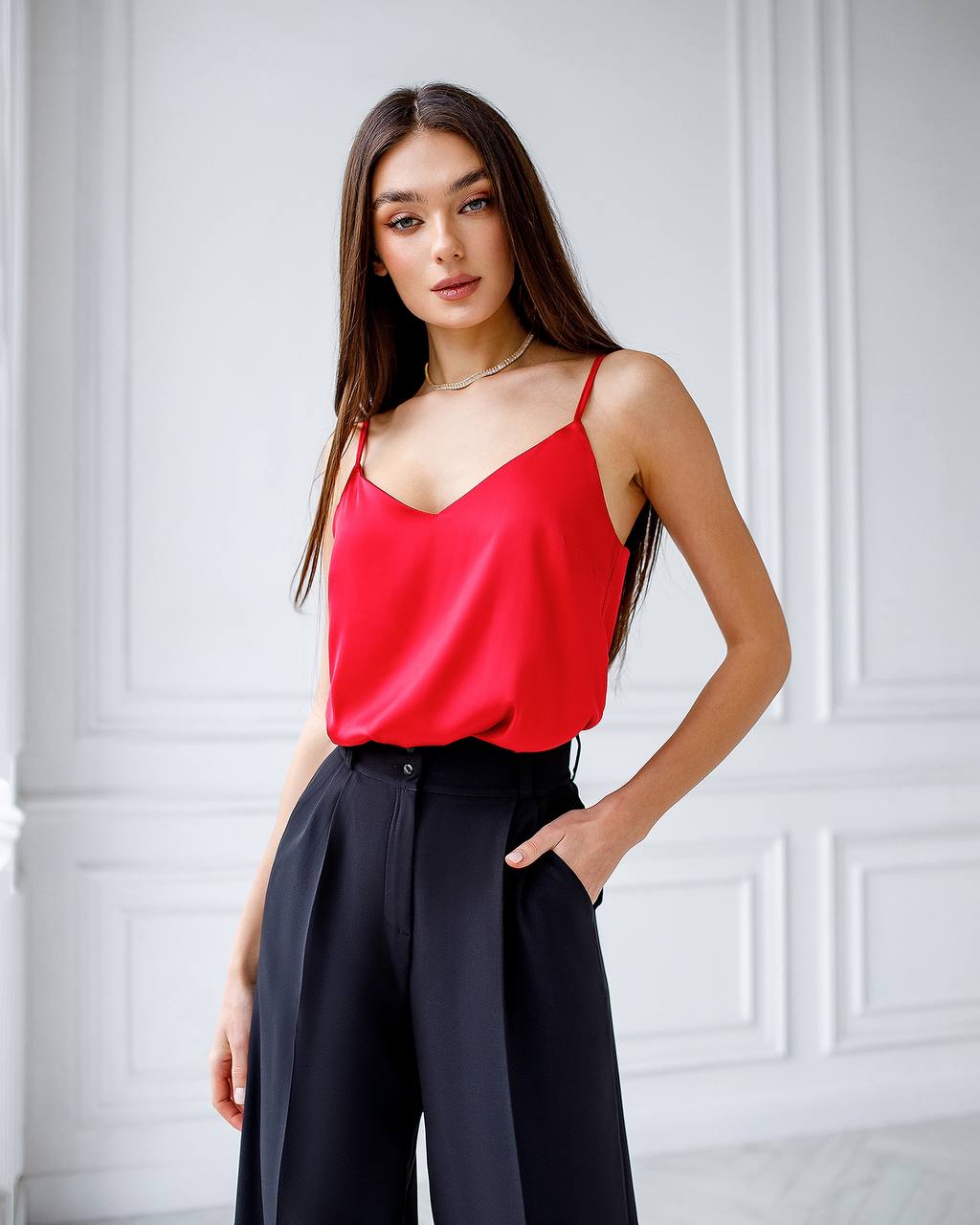 Woman wearing a red top and black pants against a white paneled wall