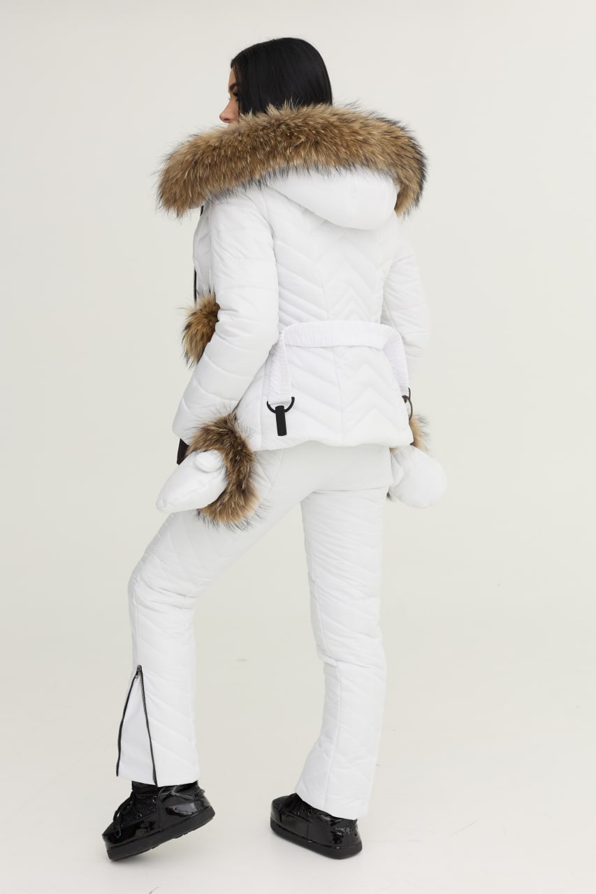 Person wearing a white winter coat with fur hood and white pants on a light background
