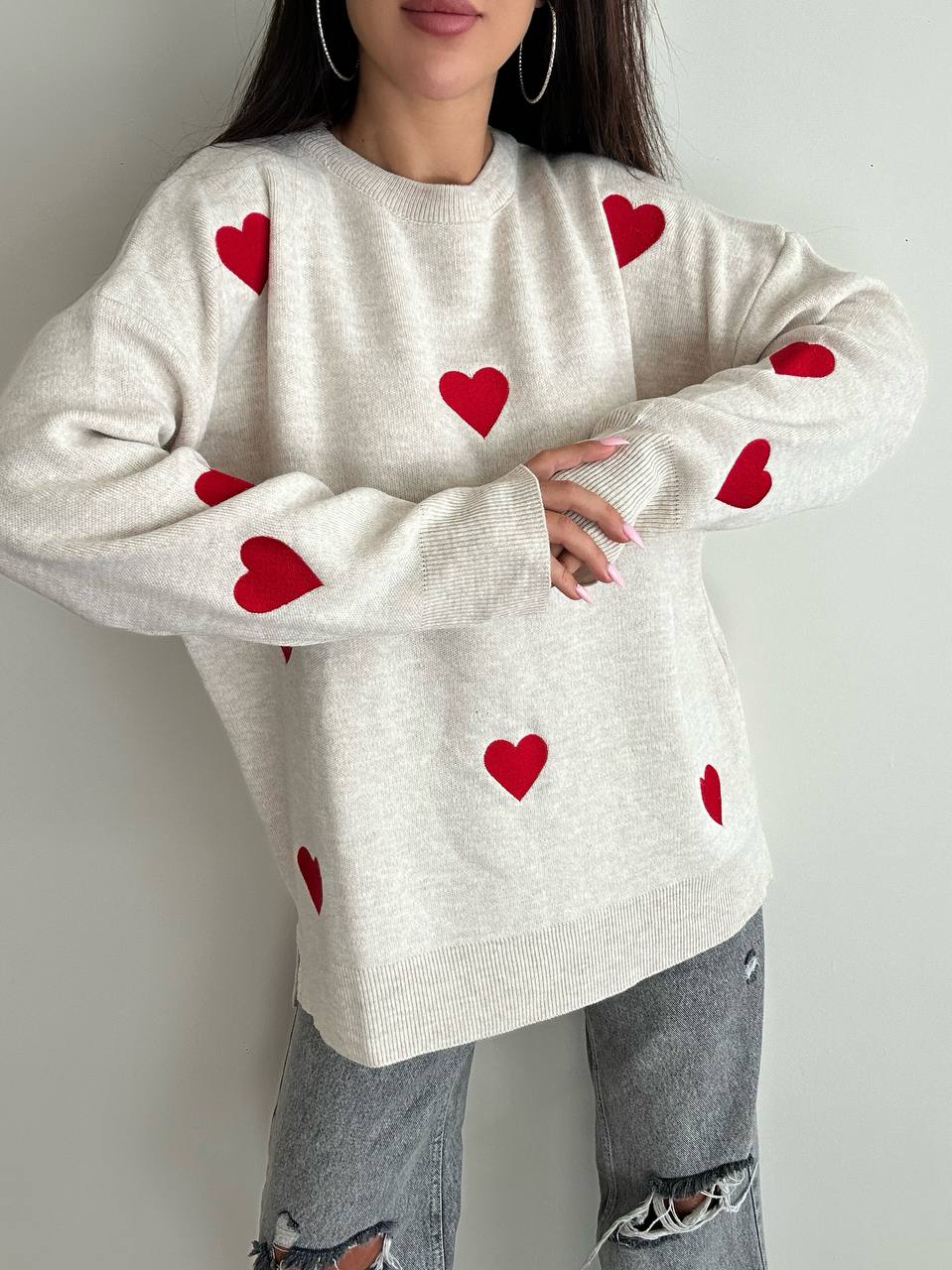 Person wearing a white sweater with red heart patterns against a plain background