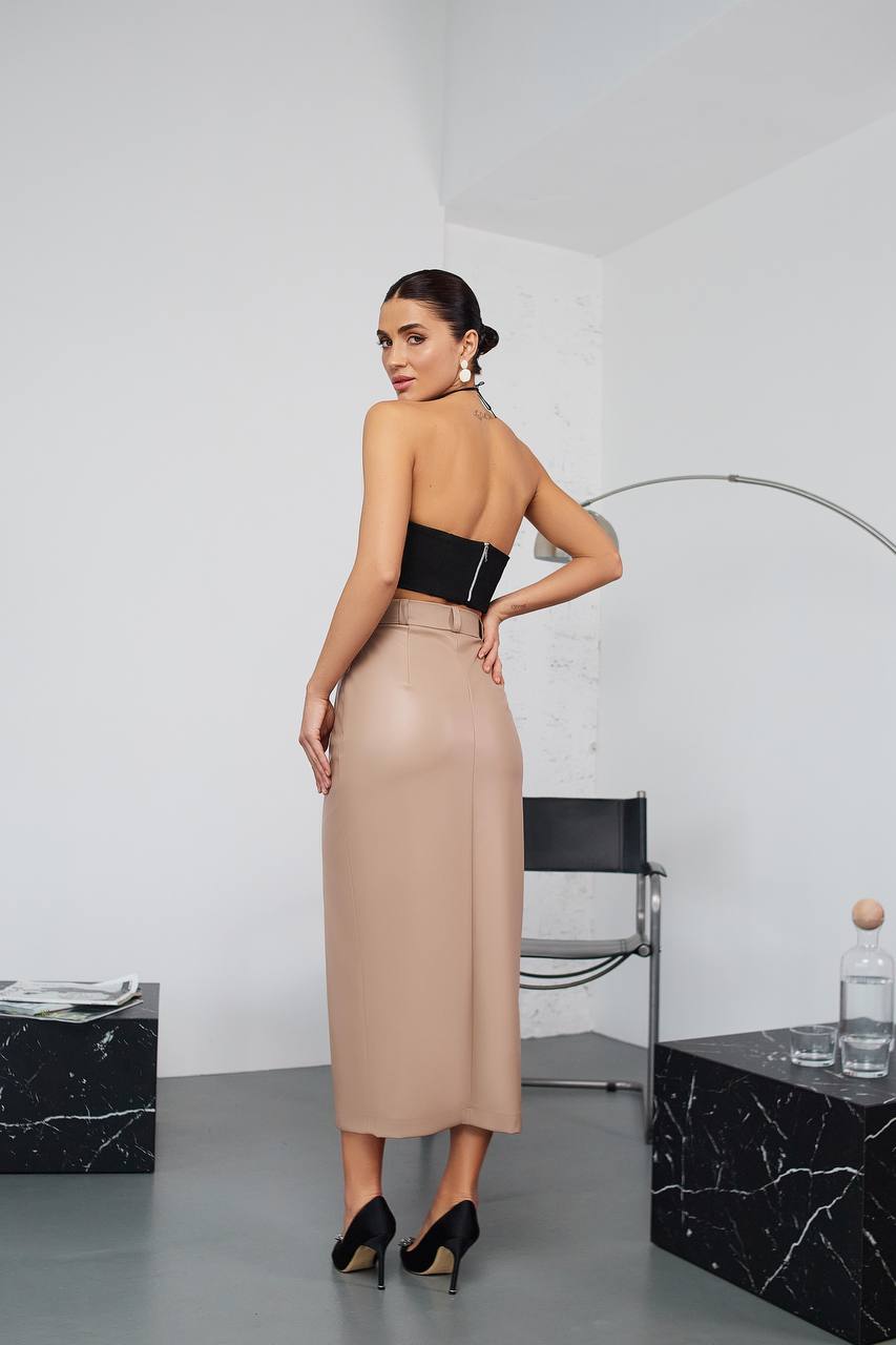 Woman in a black strapless top and beige skirt standing in a modern interior setting.