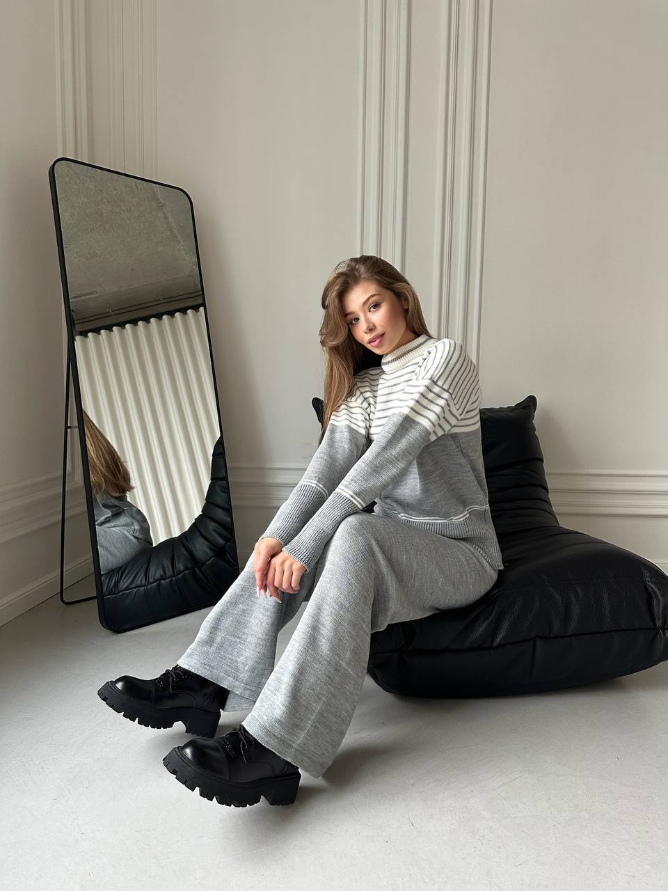 Woman sitting on a black bean bag chair in a room with a large mirror.