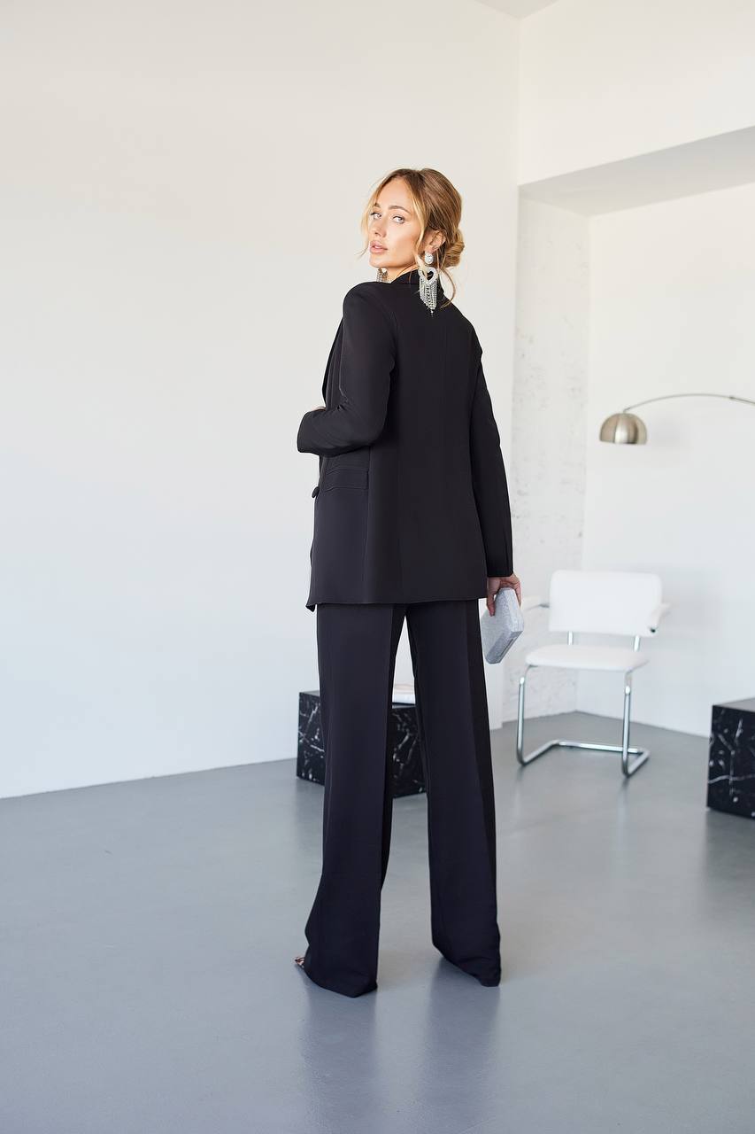 Person wearing a black suit standing in a minimalistic room with white walls and gray floor.