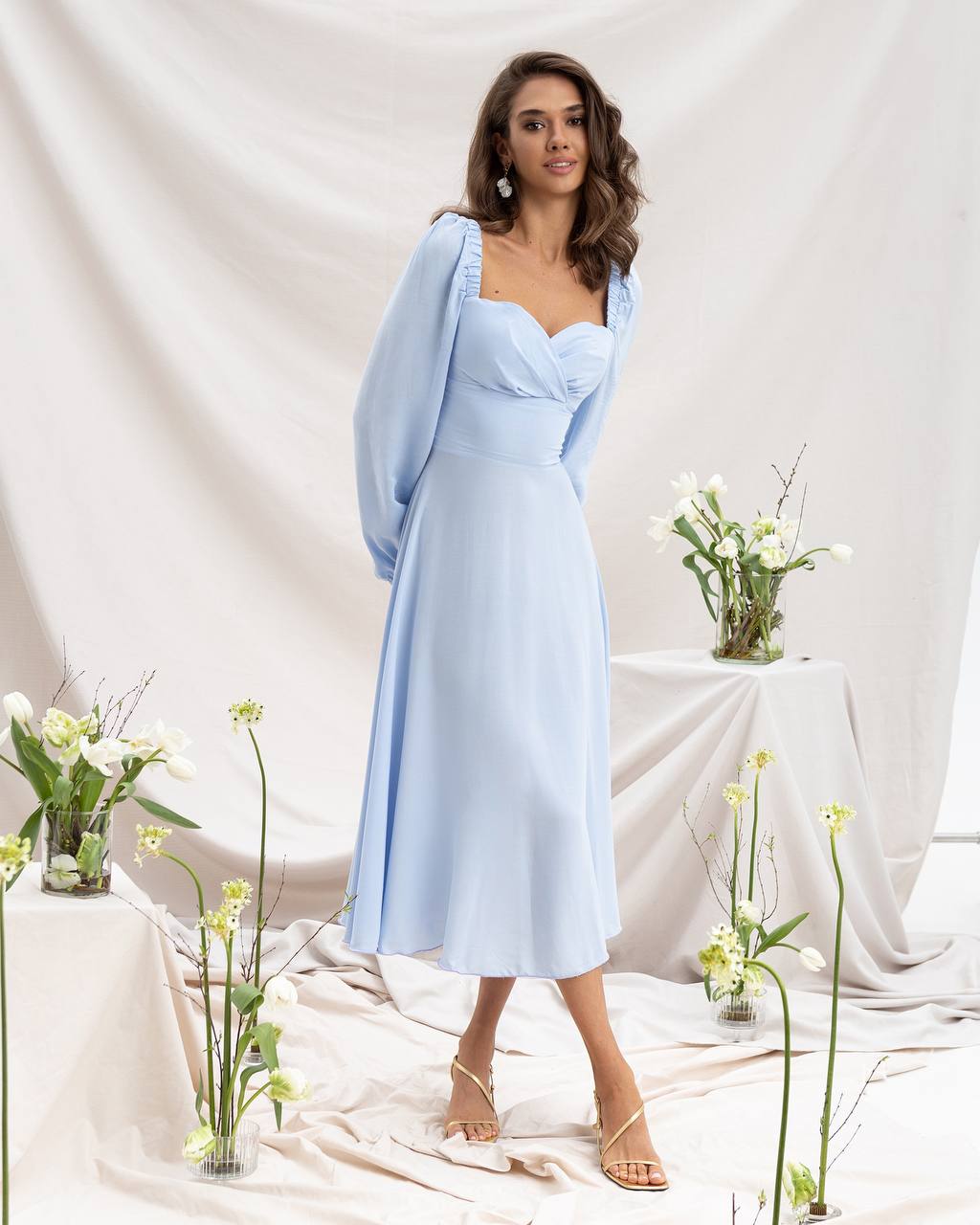 Woman in a light blue dress standing in a decorated room with flowers.