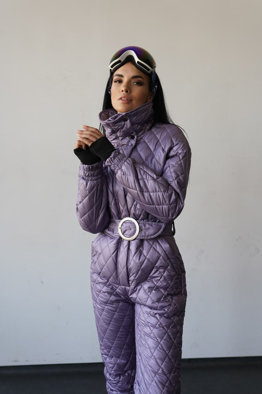 Person wearing a purple quilted snowsuit with goggles on a plain background