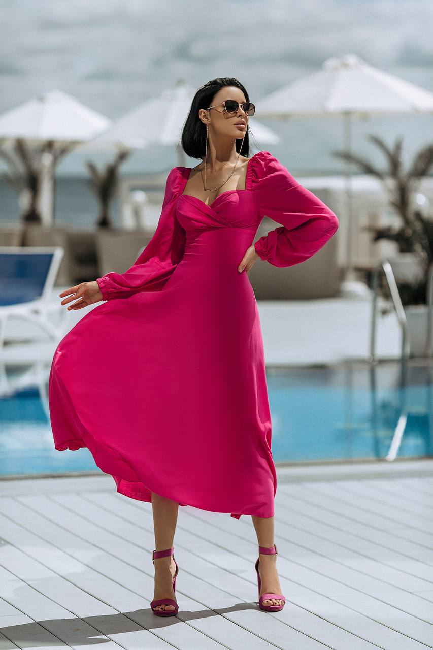 Woman in a pink dress standing by a poolside with umbrellas in the background