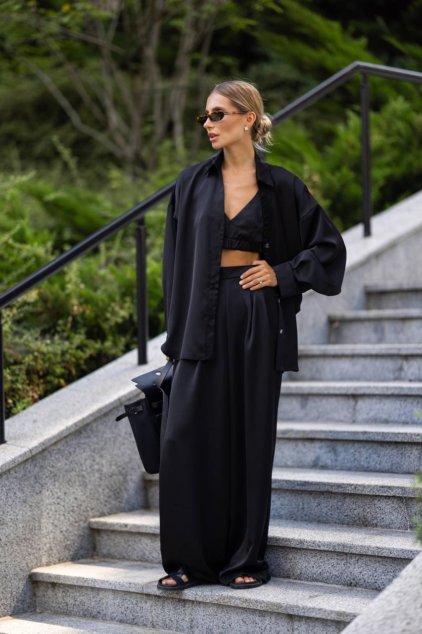 Woman in a black outfit standing on outdoor steps with greenery in the background